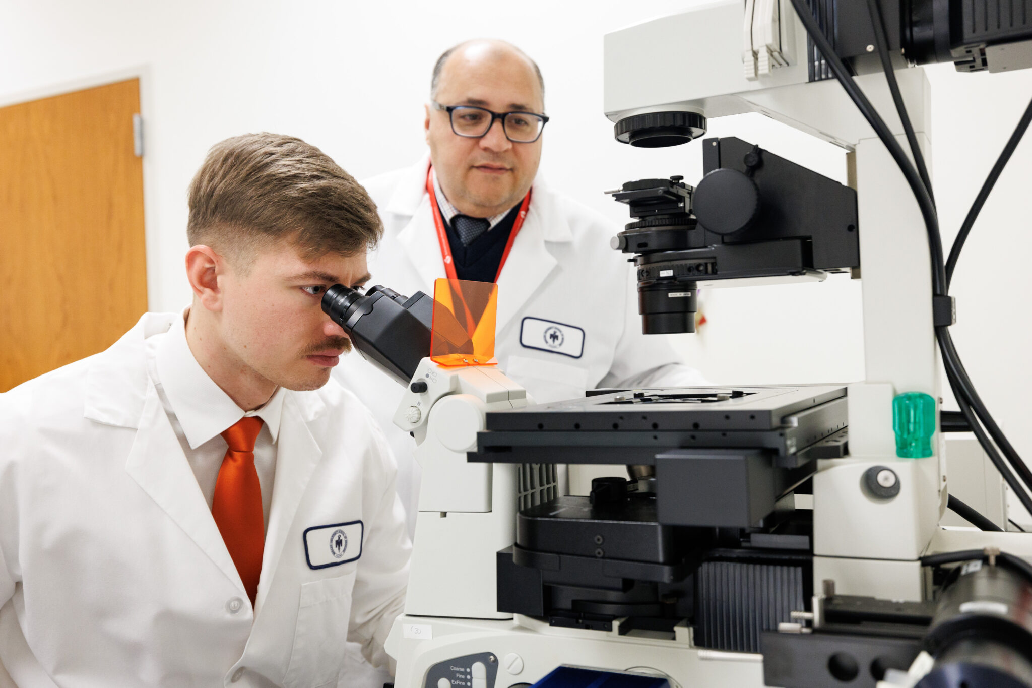 student using microscope with professor supervision