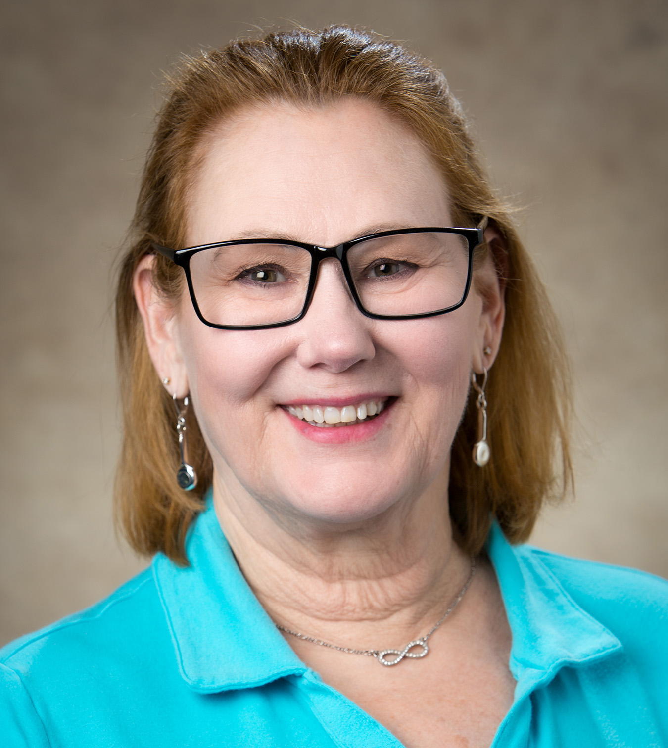 Belinda Baker in blue shirt with glasses on smiles for the camera