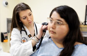 woman in white coat looks in patients ear