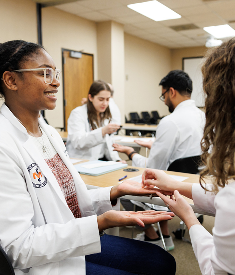 Four medical students in white coats check each others vitals