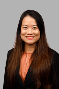 Professional headshot of smiling woman with black hair, black jacket and peach blouse.