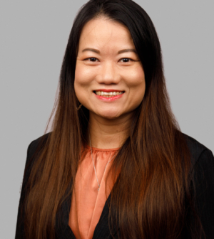 Professional headshot of smiling woman with black hair, black jacket and peach blouse.