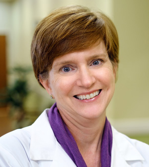 Professional headshot of smiling woman with white coat on.