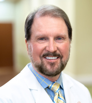 Professional headshot of smiling man with beard wearing a white coat