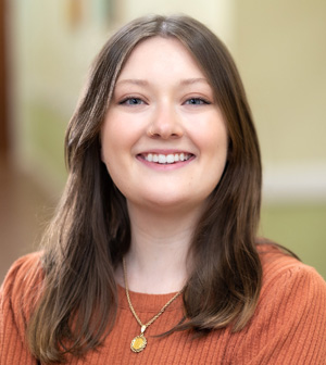 Professional headshot of smiling brunette woman with orange sweater on.