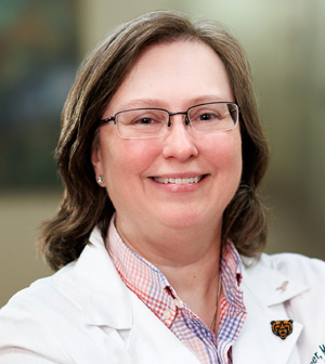 Professional headshot of smiling woman wearing glasses and a white coat.