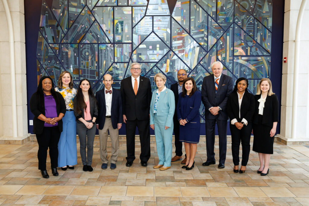 group of MFT scholars and Mercer leadership standing in front of glass mural