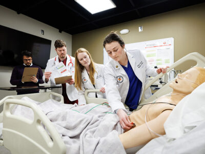 Threes students work on medical manikin while professor oversees.