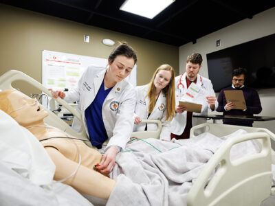 Threes students work on medical manikin while professor oversees.