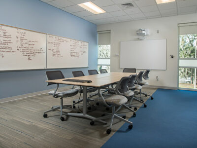Classroom with one large table and 9 chairs with whiteboards.