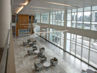 Airy lobby with chairs and tables and a long wall with floor to ceiling windows.