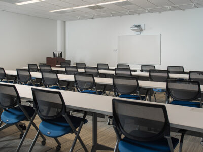 Large room with learning screens on one wall and many long tables with chairs.