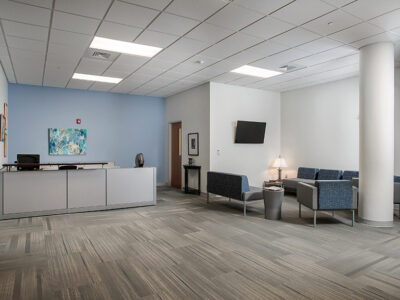 Large room with two couches, chair, lamp, side table and check in desk.