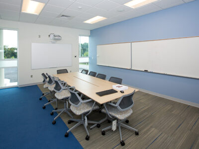 Classroom with long table and chairs and white board.