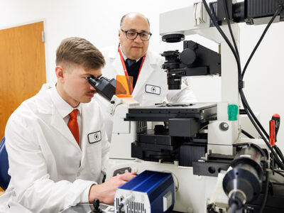 Student looking into microscope with faculty member behind him.