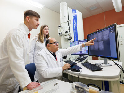 Professor pointing at the computer screen instructing 2 students.