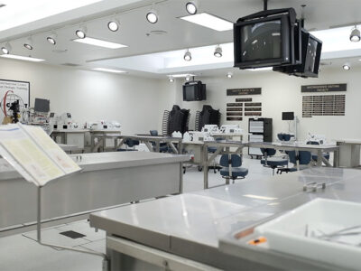 Big room with white walls, metal beds and monitors hanging from the ceiling.