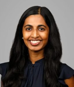 Dr. Sheila Thomas, wearing a dark blue top, smiles in front of a gray background. 