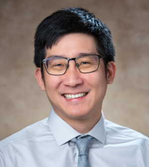 Dr. Tse-Yu Chen, wearing glasses, a light blue shirt and tie, smiles in front of a beige backdrop.
