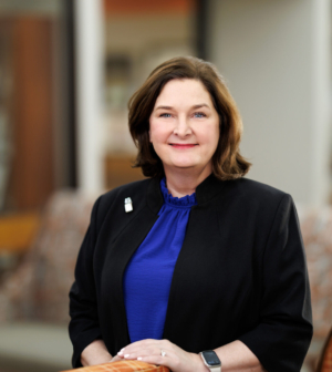 Dr. Candi Nobles-James smiling while wearing a blue shirt and black blazer in the medical school lobby.
